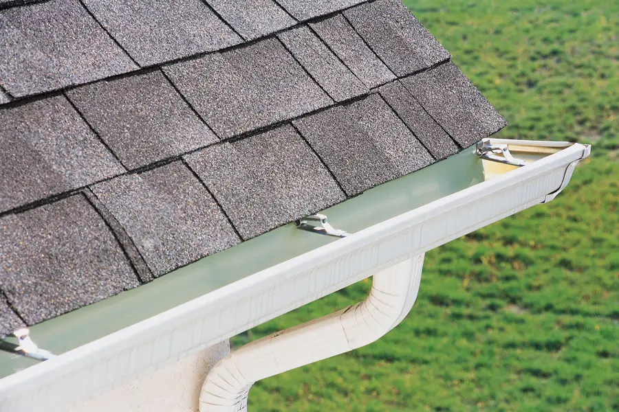 White gutter and downspout on a shingle roof edge