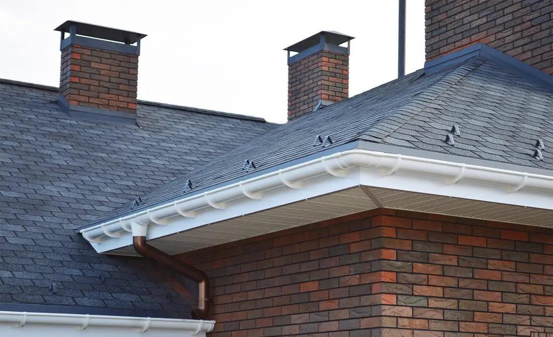 Brick chimney and a white gutter along a gray shingle roof